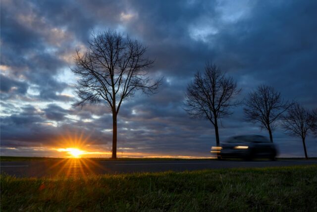 Ein Auto fährt auf einer Landstraße. Über den Himmel ziehen dunkle Wolken.