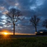 Ein Auto fährt auf einer Landstraße. Über den Himmel ziehen dunkle Wolken.