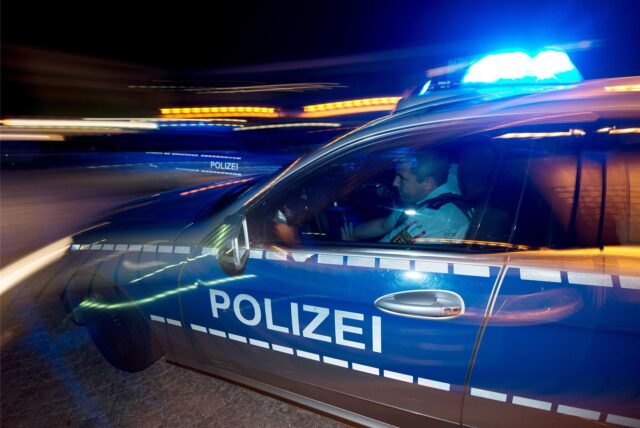 Ein Polizist sitzt in einem Streifenwagen mit eingeschaltetem Blaulicht.
