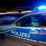 Ein Polizist sitzt in einem Streifenwagen mit eingeschaltetem Blaulicht.