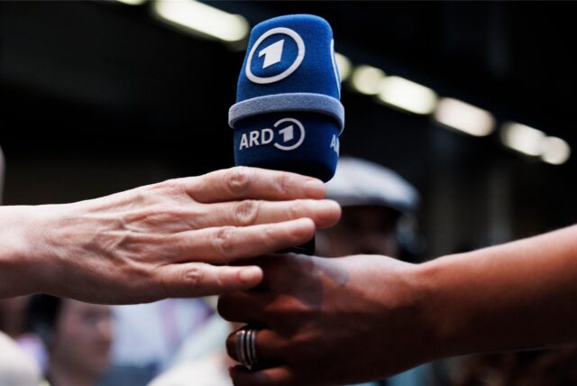 Eine Hand überreicht ein ARD-Mikrofon.