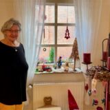 Eine Seniorin steht an einem weihnachtlich dekorierten Fenster.