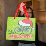 Eine Weihnachtsmarkt-Händlerin hält eine Tüte mit dem Grinch und der Aufschrift „Ich hasse Weihnachten“ in die Höhe.