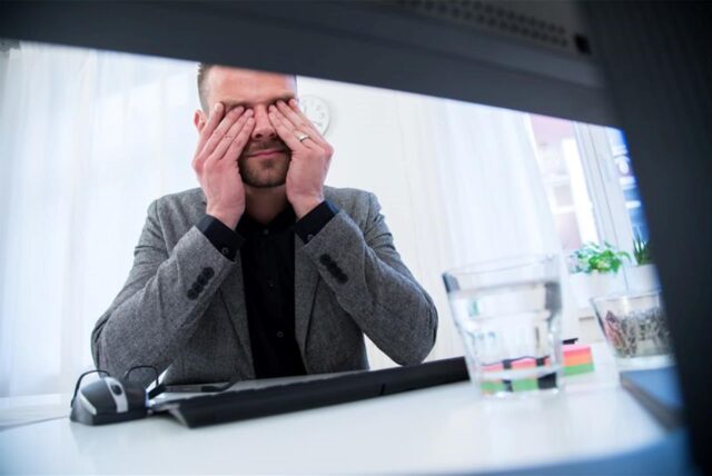 Ein Mann sitzt vor einem Computer und reibt sich die Augen.