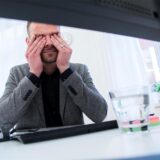 Ein Mann sitzt vor einem Computer und reibt sich die Augen.
