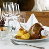 Ein festlich gedeckter Tisch, darauf ein Teller mit Gänsebraten, Klößen und Sauce