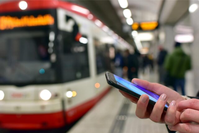 Ein Handy ist vor einer Stadtbahn in Dortmund zu sehen.