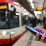 Ein Handy ist vor einer Stadtbahn in Dortmund zu sehen.
