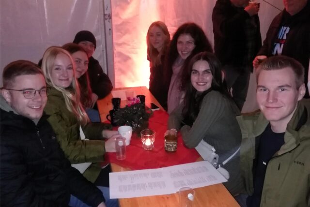 Mehrere junge Leute sitzen bei der Adventsparty in Sperckhorn an einem Biertisch und lächeln in die Kamera.