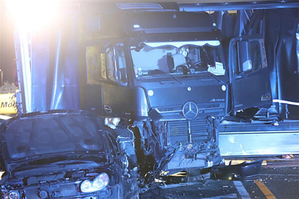 Ein Lastwagen steht auf der Autobahn 1 bei Hagen an der Unfallstelle neben einem beschädigten Auto.