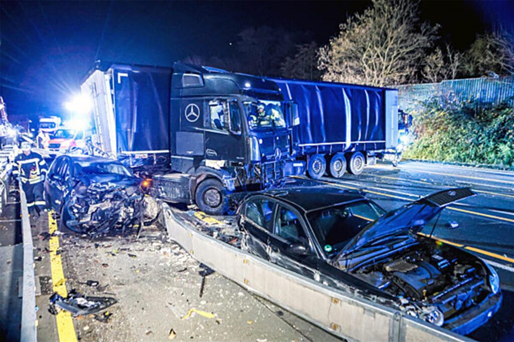 Ein Lastwagen steht auf der Autobahn 1 bei Hagen an der Unfallstelle neben beschädigten Autos.