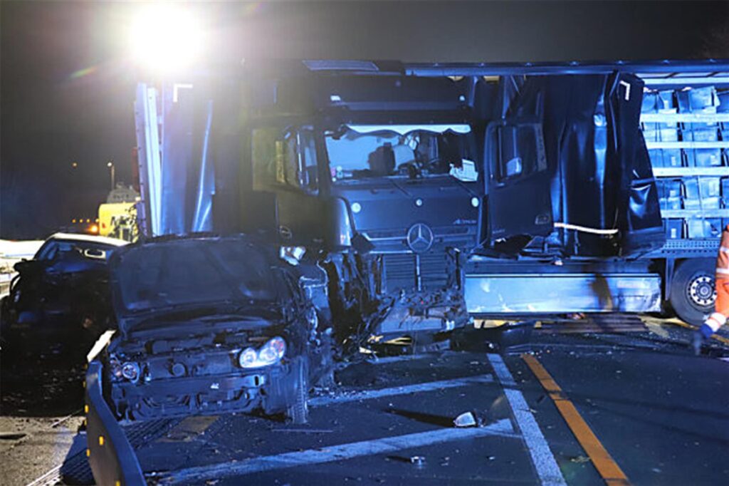 Ein Lastwagen steht auf der Autobahn 1 bei Hagen an der Unfallstelle neben beschädigten Autos.