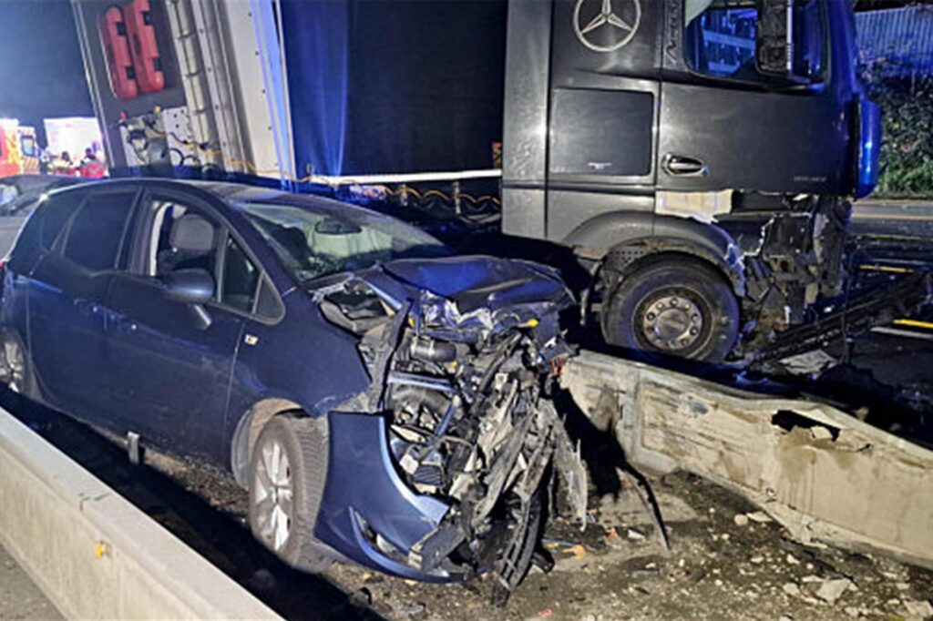 Ein Lastwagen steht auf der Autobahn 1 bei Hagen an der Unfallstelle neben beschädigten Autos.