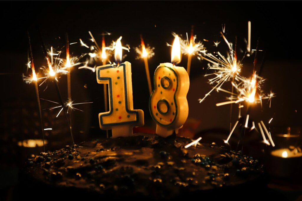 Geburtstagstorte zum 18. Geburtstag mit brennenden Kerzen in Form einer 1 und einer 8.