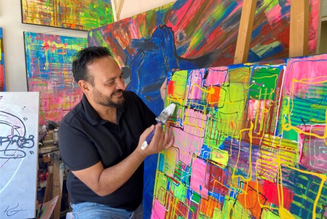 Adnan Kassim malt mit einem Pinsel weiße Farbe auf ein buntes Bild.