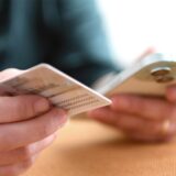 Nahaufnahme von zwei Händen, die ein Handy und einen Personalausweis halten.
