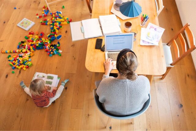 Eine Mutter sitzt am Tisch und arbeitet am Laptop, während ein Kind neben ihr auf dem Boden sitzt und spielt.Ein Minijob in der Elternzeit bringt Vorteile – aber nur unter bestimmten Bedingungen. Nicht jede Art von Minijob lässt sich während der Elternzeit ohne Weiteres ausüben. Was Sie beachten sollten.