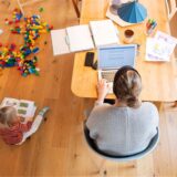 Eine Mutter sitzt am Tisch und arbeitet am Laptop, während ein Kind neben ihr auf dem Boden sitzt und spielt.Ein Minijob in der Elternzeit bringt Vorteile – aber nur unter bestimmten Bedingungen. Nicht jede Art von Minijob lässt sich während der Elternzeit ohne Weiteres ausüben. Was Sie beachten sollten.
