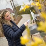 Eine Frau steht an einem geöffneten Briefkasten und schaut auf einen Brief.