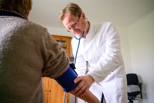 Ein Hausarzt misst den Blutdruck bei einer Patientin.