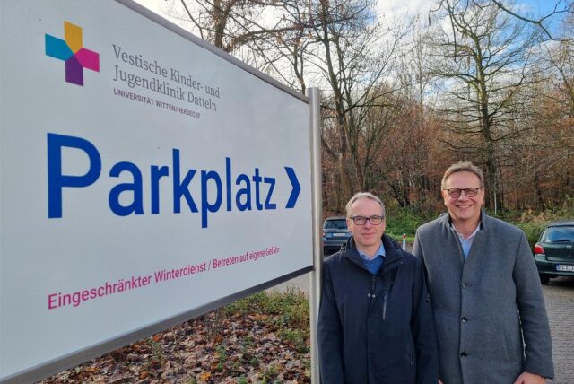 Zwei Männer stehen an einem Parkplatzschild an der Kinderklinik.