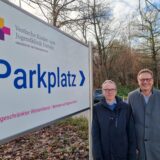 Zwei Männer stehen an einem Parkplatzschild an der Kinderklinik.