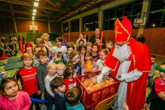 Ein Mann im Nikolaus-Kostüm steht in einer Dortmunder Turnhalle und verteilt Backteilchen an die um ihn herum stehenden Kinder.