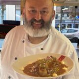 Imbissbesitzer Peter Finke von Hähnchen Finke in Dorsten hält einen Teller mit seiner Dubai-Currywurst in der Hand.