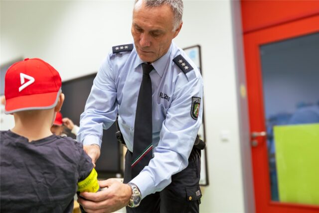 Ein Polizist der Kreispolizeibehörde in Recklinghausen legt einem Schulkind eine Leuchtbinde an.