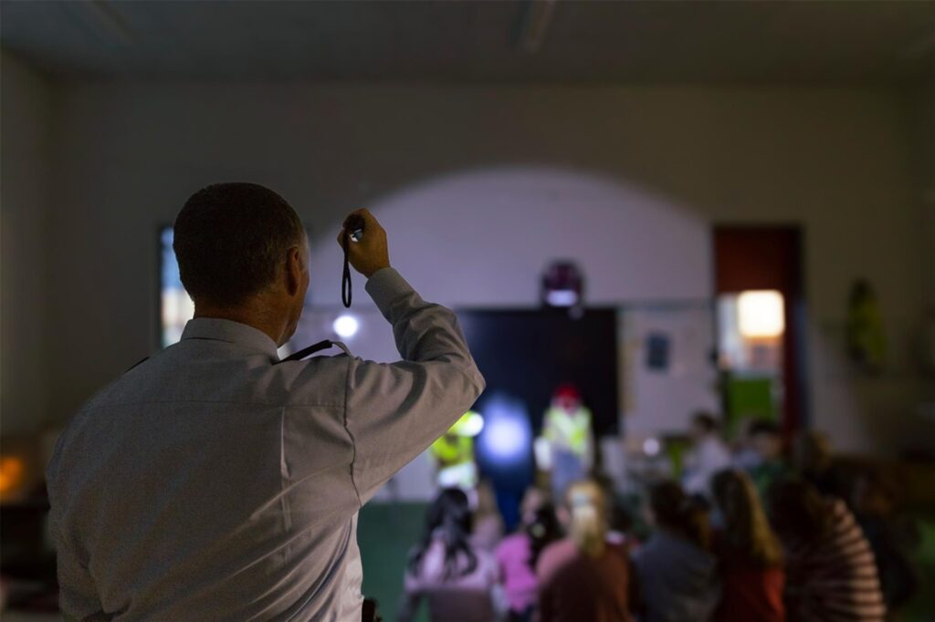 Ein Polizeibeamter zeigt Grundschülern die Wirksamkeit von Reflektoren in einem abgedunkelten Klassenraum. Ein Polizeibeamter zeigt Grundschülern die Wirksamkeit von Reflektoren in einem abgedunkelten Klassenraum.