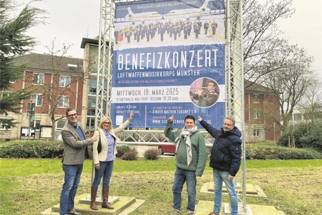 Vier Leute zeigen vor dem Waltroper Rathaus auf ein Werbeplakat für ein Benefizkonzert.