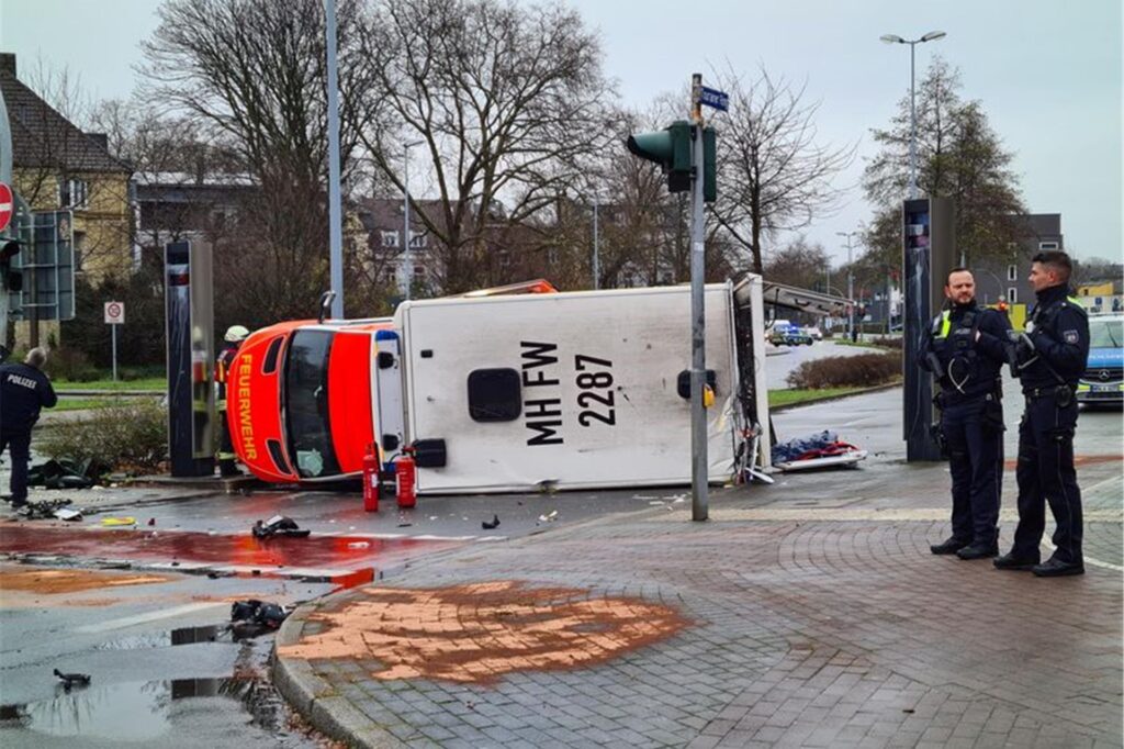 Ein Rettungswagen liegt in Mülheim an der Ruhr auf der Seite, Polizeibeamte stehen daneben.
