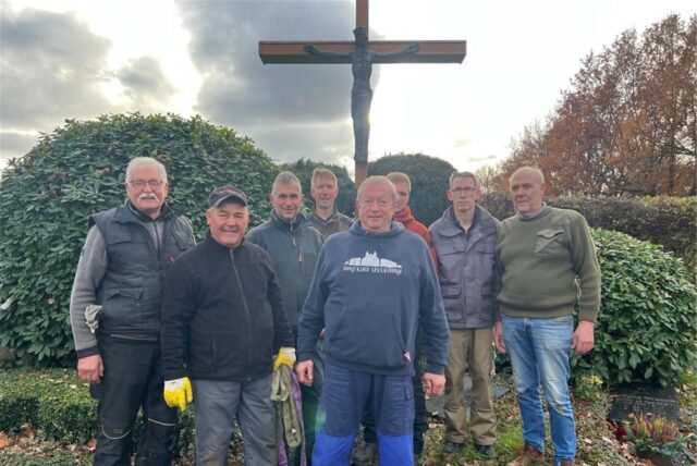 Acht Helfer stehen nach vollendeter Tat vor dem neuen Holzkreuz auf dem Friedhof in Recklinghausen-Speckhorn
