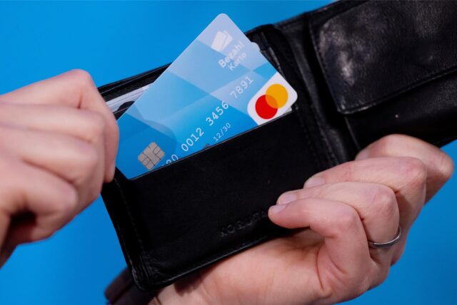 Ein Mann hält eine blaue Bezahlkarte in der Hand, die er aus einem schwarzen Portemonnaie zieht.