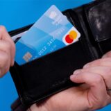 Ein Mann hält eine blaue Bezahlkarte in der Hand, die er aus einem schwarzen Portemonnaie zieht.