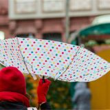 Eine Frau geht mit einem Regenschirm über den Weihnachtsmarkt.