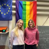 Zwei Frauen stehen im Klassenraum im Theodor-Heuss-Gymnasium in Waltrop vor einer Regenbogen-Flagge.