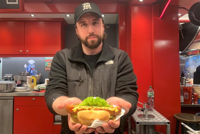 Ein Mitarbeiter eines Standes auf dem Dortmunder Weihnachtsmarkt hält eine vegane Bratwurst im Brötchen in den Händen.
