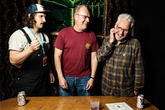 Sebastian Vorhölter, Dominik Sprenger und Martin Hoppe stehen an einem Tisch und lachen.