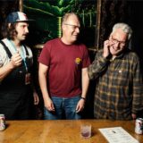 Sebastian Vorhölter, Dominik Sprenger und Martin Hoppe stehen an einem Tisch und lachen.
