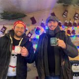 Zwei Aussteller stehen mit Glühweintassen in den Händen in ihrer Bude.