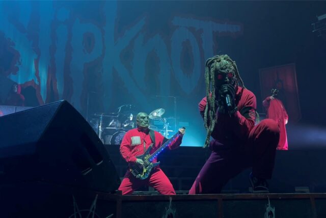 Der Sänger von Slipknot steht am Bühnenrand und singt, im Hintergrund stehen einer der Gitarristen und das Schlagzeug.