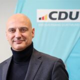 Alexander Kalouti lächelt in die Kamera, vor einem Logo der CDU