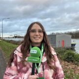 Redakteurin Lara Teschers steht am Kanal und hält ein Mikrofon in der Hand.