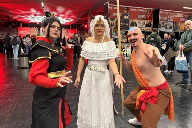 Zwei Frauen und ein Mann haben sich verkleidet. Der Mann sieht aus wie der kleine Avatar, mit blauem Pfeil auf dem Kopf. Die Frauen tragen ebenfalls Kostüme.
