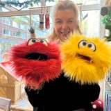 Susanne Wenzel hält eine kuschelige rote und gelbe Handpuppe in ihren Händen.