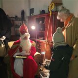 Der Nikolaus sitzt im Sessel und unterhält sich mit einem Kind und einer Frau. Im Hintergrund steht Knecht Ruprecht.
