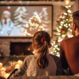 Ein Vater und seine Tochter sitzen in einem weihnachtlich geschmückten Wohnzimmer und genießen das TV-Programm an Weihnachten.