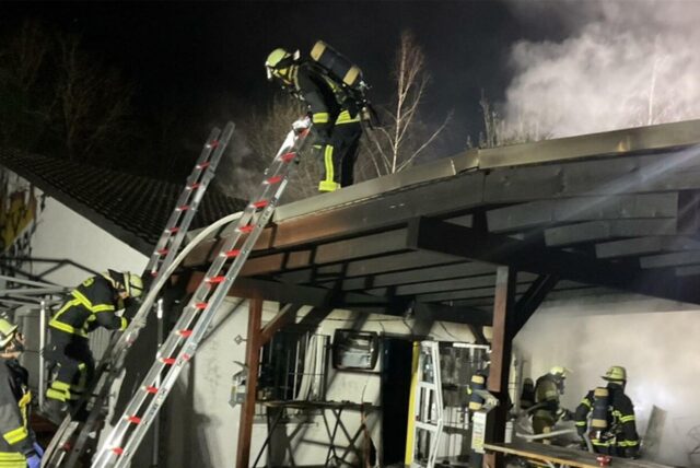 Mehrere Feuerwehrleute sind unter, auf und neben einem qualmenden Vordach.