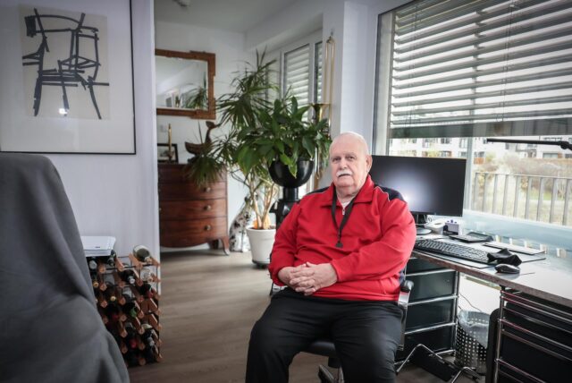 Jürgen (83) sitzt auf einem Bürostuhl an seinem Schreibtisch im Apartment.